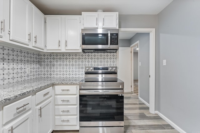 kitchen featuring appliances with stainless steel finishes, hardwood / wood-style flooring, light stone countertops, decorative backsplash, and white cabinets