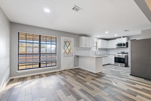 kitchen with sink, white cabinetry, light wood-type flooring, appliances with stainless steel finishes, and decorative backsplash