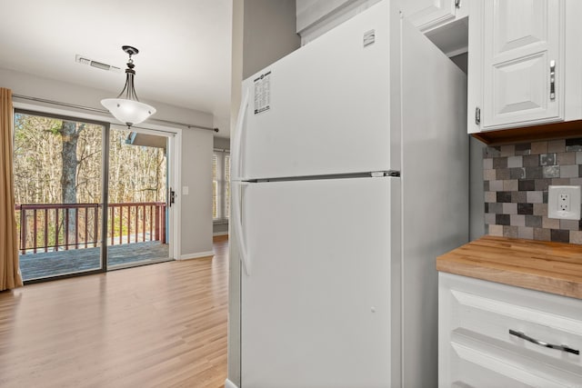 kitchen with white cabinets, decorative backsplash, hanging light fixtures, white fridge, and a healthy amount of sunlight