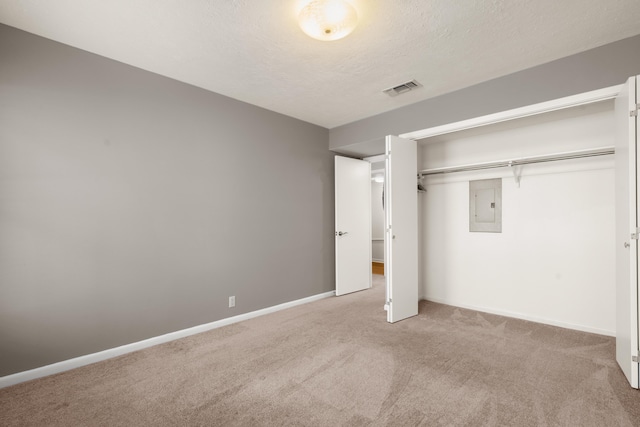 unfurnished bedroom with light colored carpet, electric panel, a closet, and a textured ceiling