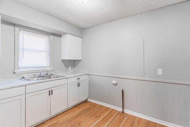 kitchen with white cabinetry, sink, a textured ceiling, and light wood-type flooring