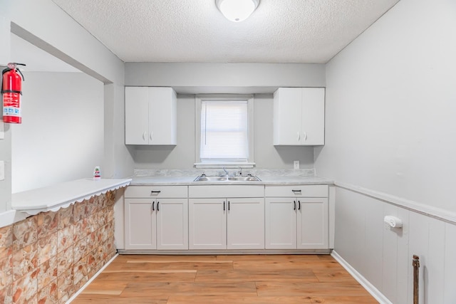 kitchen featuring sink, a textured ceiling, white cabinets, and light wood-type flooring