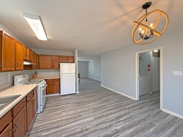 kitchen featuring white appliances, decorative light fixtures, washer / dryer, and light wood-type flooring