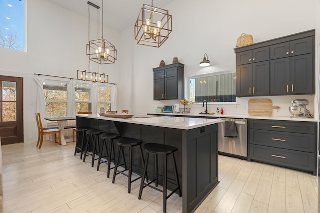 kitchen with a kitchen bar, a center island, hanging light fixtures, light hardwood / wood-style flooring, and stainless steel dishwasher