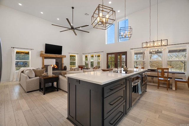 kitchen featuring a stone fireplace, french doors, an island with sink, stainless steel appliances, and light hardwood / wood-style flooring