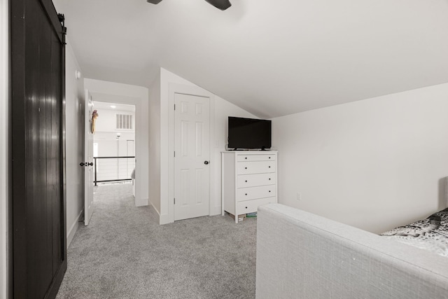 unfurnished bedroom with light carpet, vaulted ceiling, a barn door, and ceiling fan