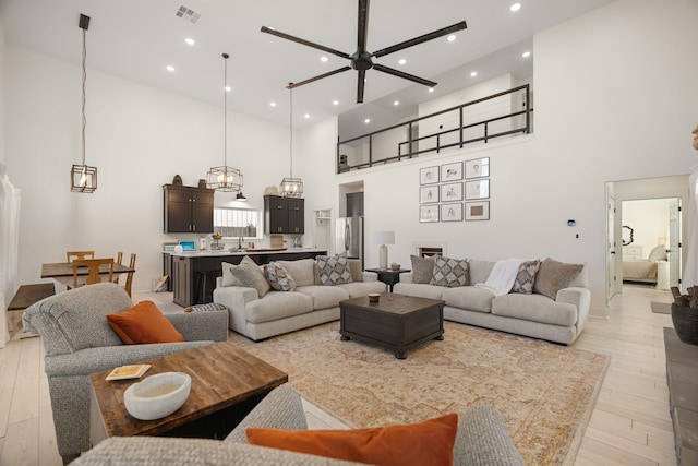 living room with sink, a towering ceiling, light hardwood / wood-style flooring, and ceiling fan