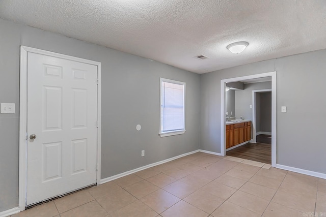 empty room featuring sink, a textured ceiling, and light tile patterned floors