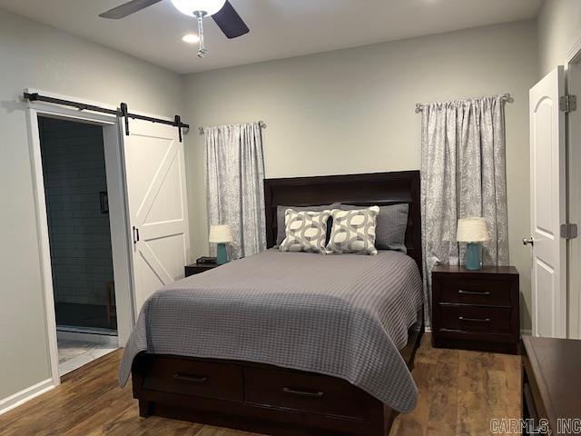 bedroom featuring a barn door, dark wood-type flooring, and ceiling fan