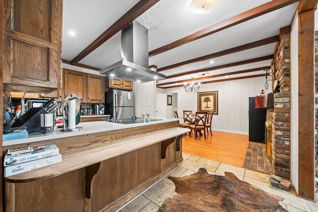 kitchen featuring kitchen peninsula, a notable chandelier, beamed ceiling, island exhaust hood, and black appliances