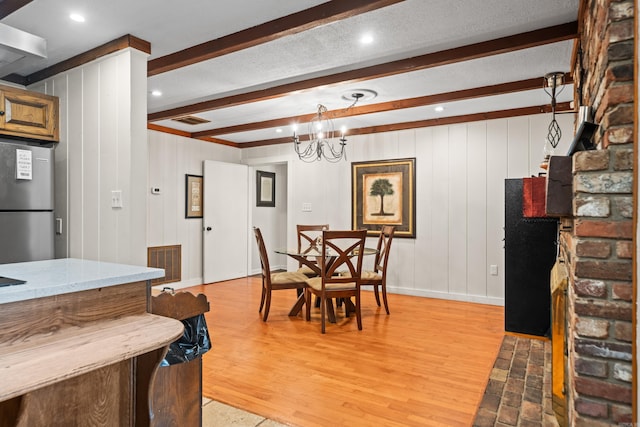 dining space with an inviting chandelier, a textured ceiling, light hardwood / wood-style flooring, and beamed ceiling