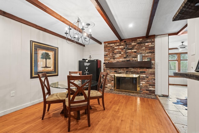 dining room featuring beamed ceiling, a brick fireplace, a textured ceiling, and light hardwood / wood-style flooring