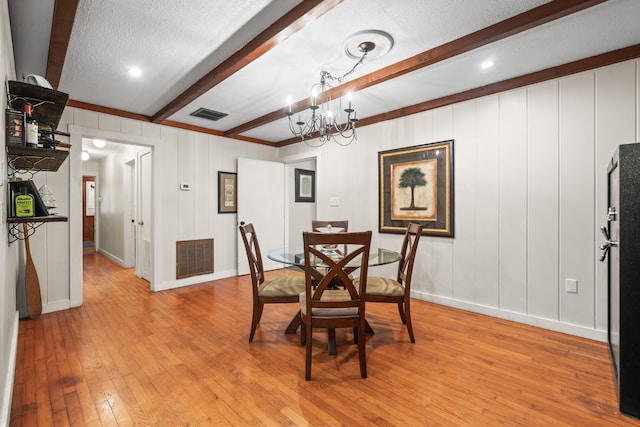 dining room featuring beamed ceiling, an inviting chandelier, light hardwood / wood-style floors, and a textured ceiling