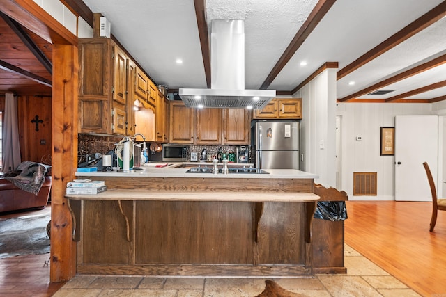 kitchen featuring a breakfast bar, kitchen peninsula, beamed ceiling, island exhaust hood, and stainless steel appliances