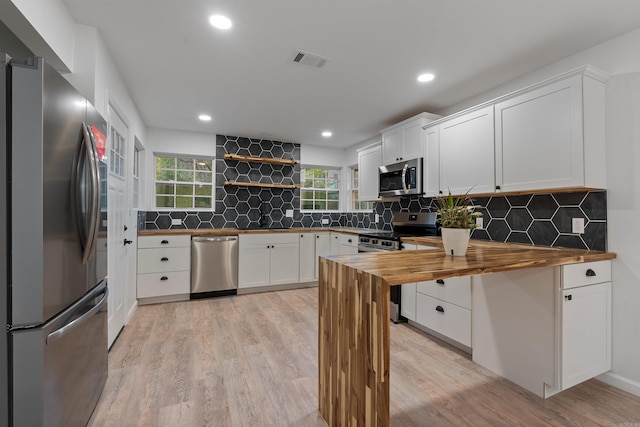 kitchen with light hardwood / wood-style floors, stainless steel appliances, wooden counters, and white cabinets