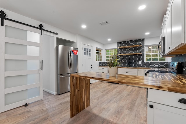 kitchen featuring stainless steel appliances, wooden counters, white cabinets, and a barn door