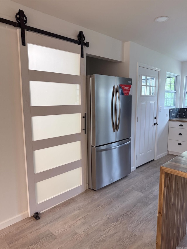 kitchen featuring white cabinetry, a barn door, light wood-type flooring, and stainless steel refrigerator