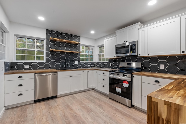 kitchen with appliances with stainless steel finishes, butcher block counters, white cabinets, decorative backsplash, and light hardwood / wood-style floors