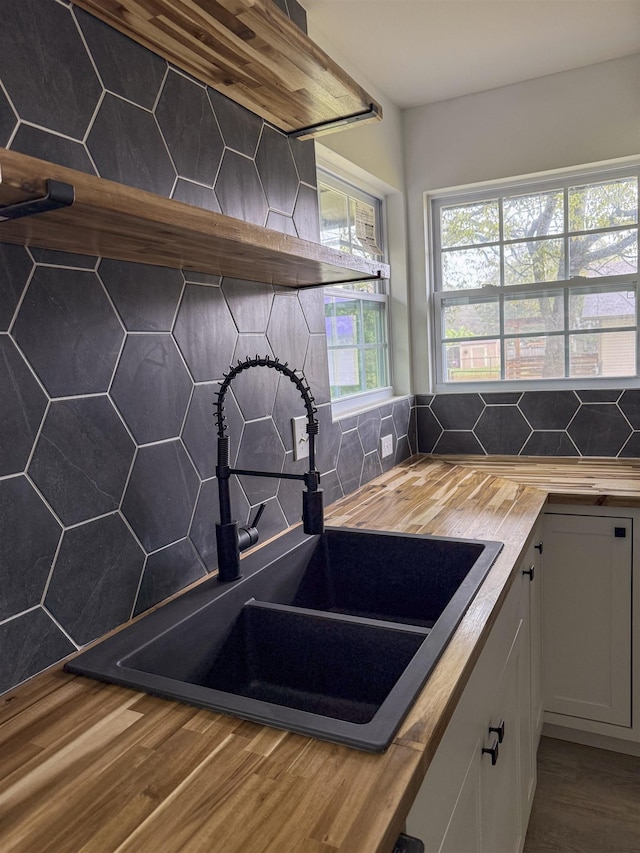 kitchen featuring sink, butcher block counters, backsplash, white cabinetry, and wood-type flooring