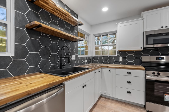 kitchen featuring white cabinetry, sink, butcher block counters, backsplash, and stainless steel appliances