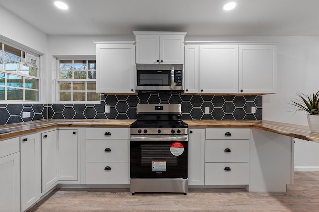 kitchen featuring appliances with stainless steel finishes, backsplash, white cabinets, wood counters, and light wood-type flooring