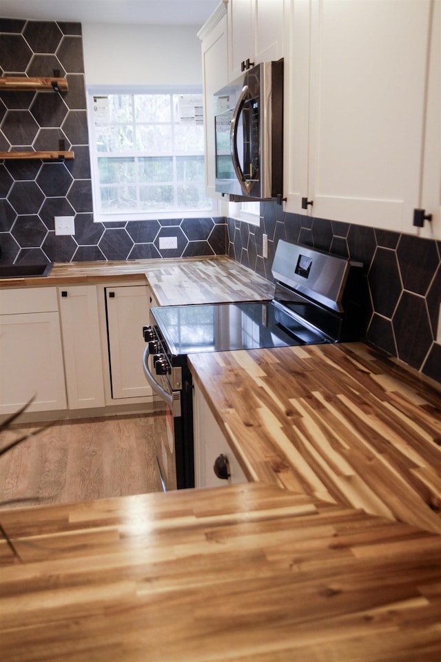 kitchen with white cabinetry, appliances with stainless steel finishes, butcher block countertops, and tasteful backsplash