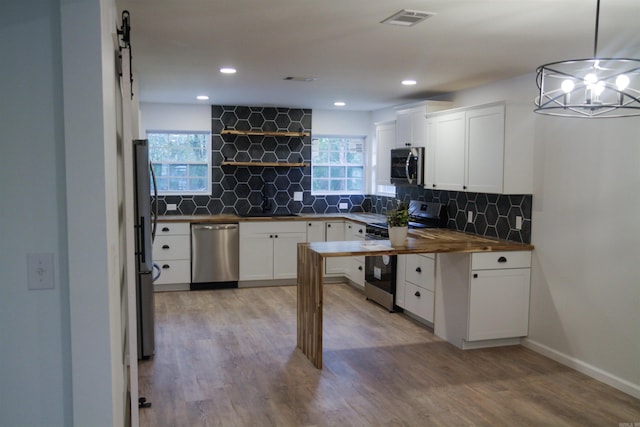 kitchen featuring butcher block counters, pendant lighting, stainless steel appliances, and white cabinetry