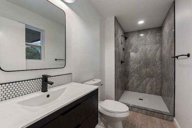 bathroom featuring toilet, a tile shower, vanity, hardwood / wood-style floors, and decorative backsplash