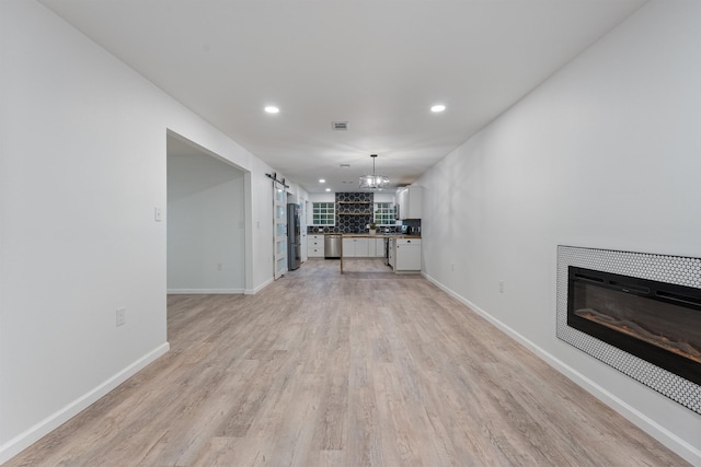 unfurnished living room featuring a barn door and light hardwood / wood-style flooring