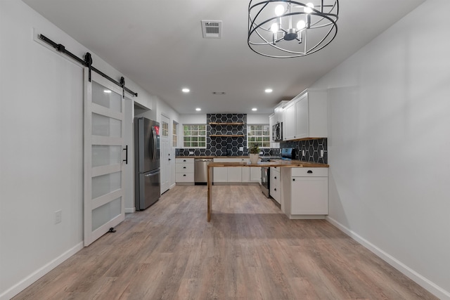 kitchen featuring pendant lighting, butcher block countertops, appliances with stainless steel finishes, white cabinets, and a barn door