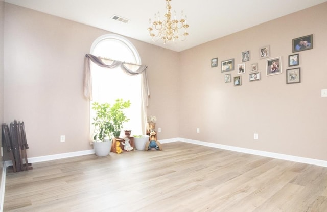 empty room featuring a notable chandelier and light wood-type flooring