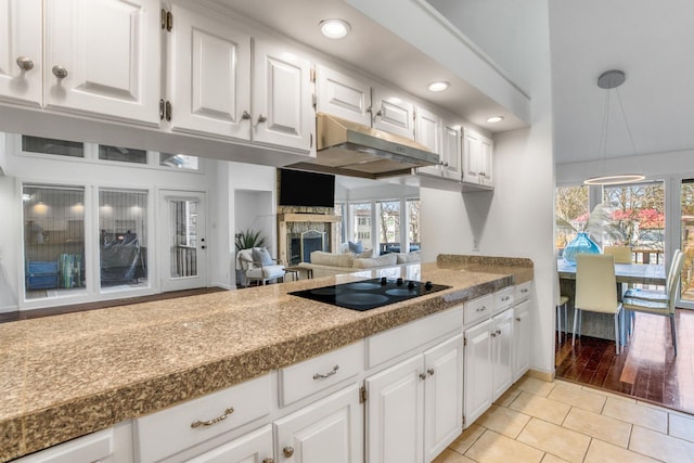 kitchen featuring a stone fireplace, white cabinetry, hanging light fixtures, light tile patterned floors, and black electric cooktop