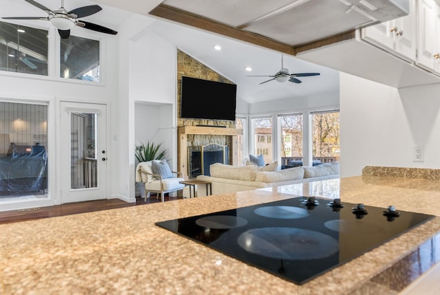 kitchen with ceiling fan, beam ceiling, high vaulted ceiling, a fireplace, and black electric cooktop