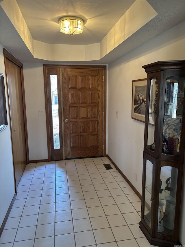 entryway featuring light tile patterned floors, a tray ceiling, and a textured ceiling