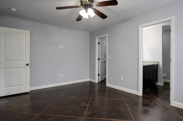 unfurnished bedroom with ceiling fan, dark tile patterned floors, and ensuite bathroom