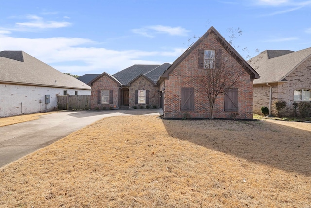 view of front facade with brick siding, fence, and roof with shingles