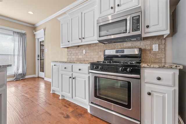 kitchen with light stone countertops, ornamental molding, stainless steel appliances, and white cabinets