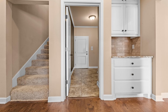 interior space featuring white cabinetry, wood-type flooring, ornamental molding, light stone countertops, and backsplash