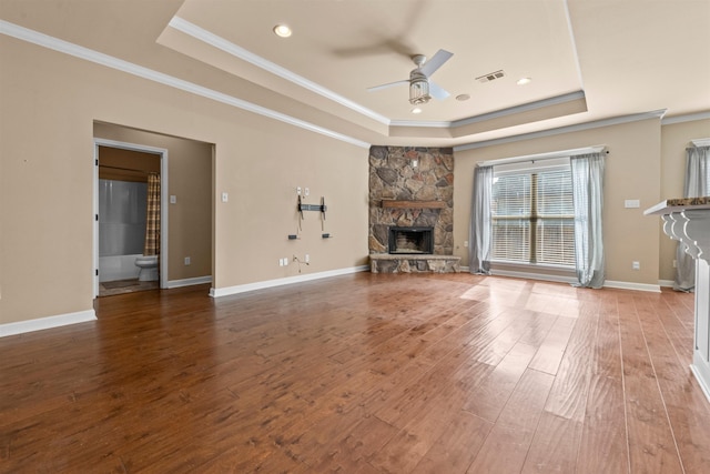 unfurnished living room with ceiling fan, a stone fireplace, a raised ceiling, and hardwood / wood-style floors