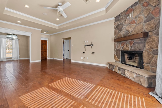 unfurnished living room with a stone fireplace, hardwood / wood-style flooring, ornamental molding, ceiling fan, and a tray ceiling