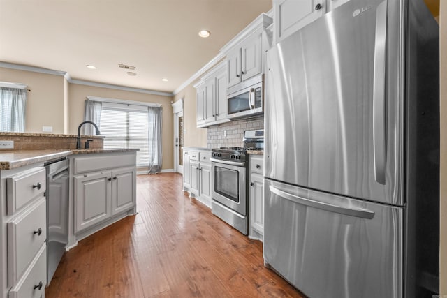 kitchen with stainless steel appliances, white cabinetry, backsplash, and crown molding