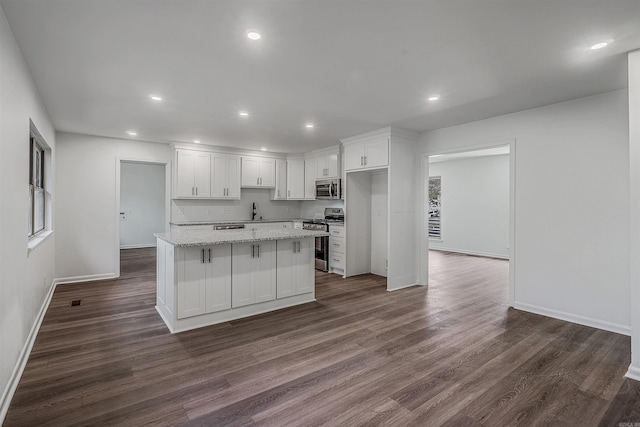 kitchen with white cabinetry, light stone counters, a center island, dark hardwood / wood-style floors, and stainless steel appliances