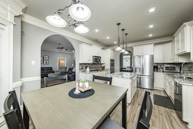 dining space with sink, crown molding, ceiling fan with notable chandelier, and light wood-type flooring