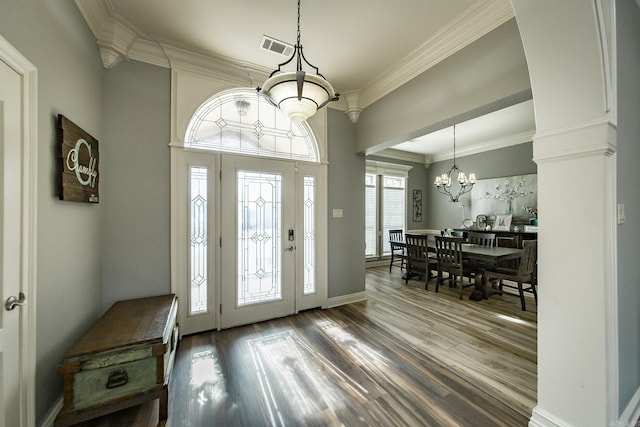 entryway with hardwood / wood-style flooring, ornamental molding, decorative columns, and a notable chandelier