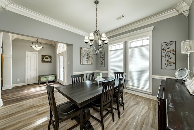 dining area with decorative columns, crown molding, a notable chandelier, and light hardwood / wood-style flooring