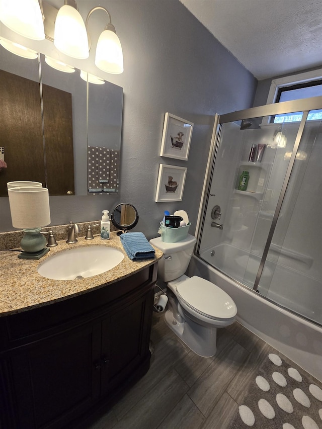 full bathroom with wood-type flooring, enclosed tub / shower combo, vanity, toilet, and a textured ceiling