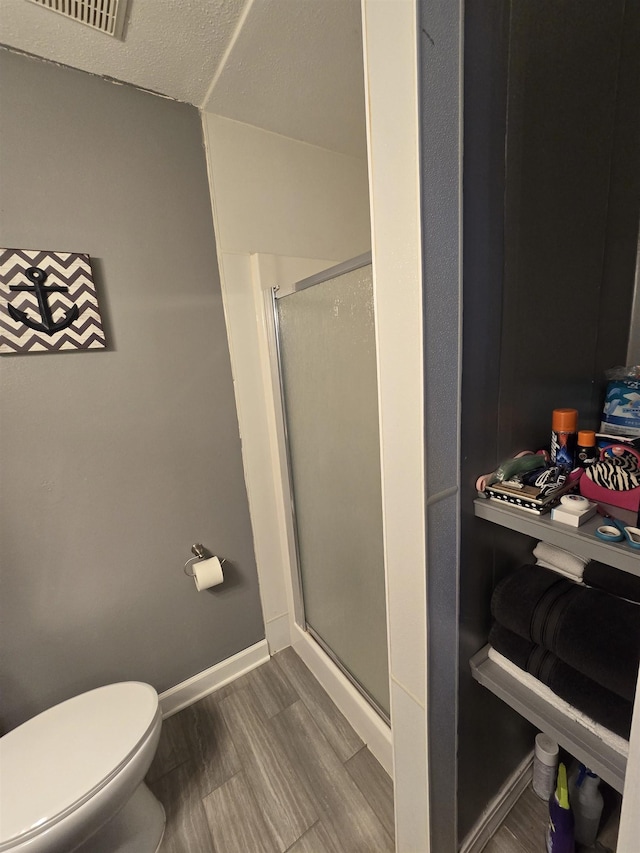 bathroom featuring hardwood / wood-style flooring, a shower with door, and toilet