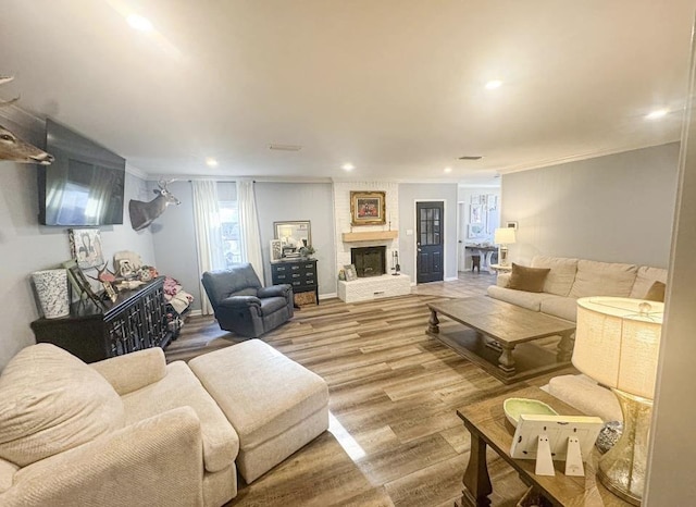 living room with wood-type flooring, a large fireplace, a wealth of natural light, and crown molding