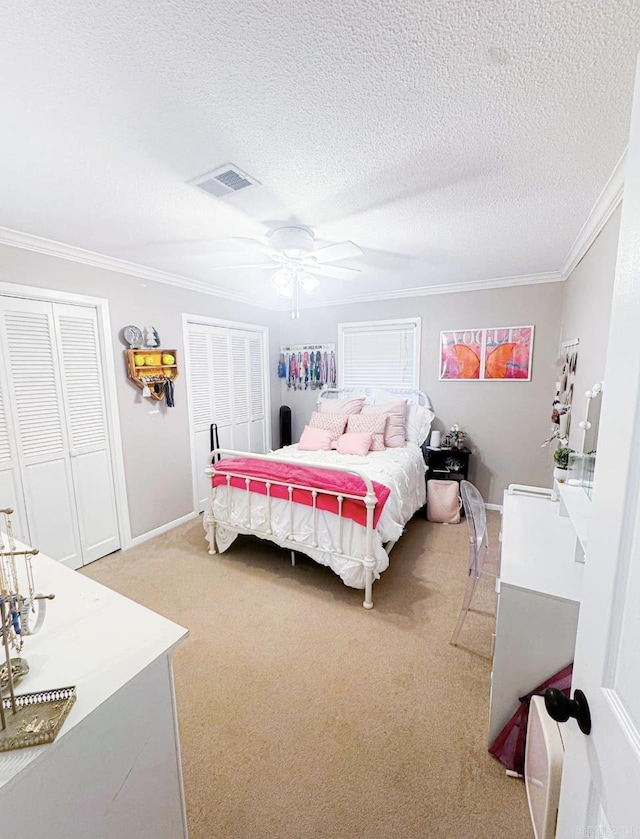 carpeted bedroom with ceiling fan, crown molding, multiple closets, and a textured ceiling