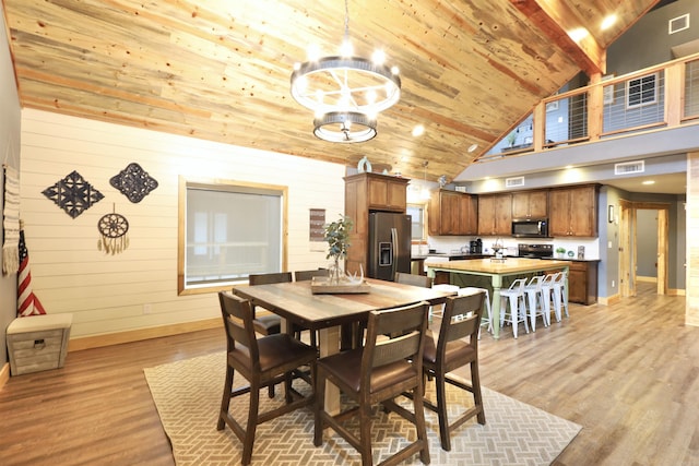 dining area with wood walls, high vaulted ceiling, wooden ceiling, a notable chandelier, and light hardwood / wood-style floors